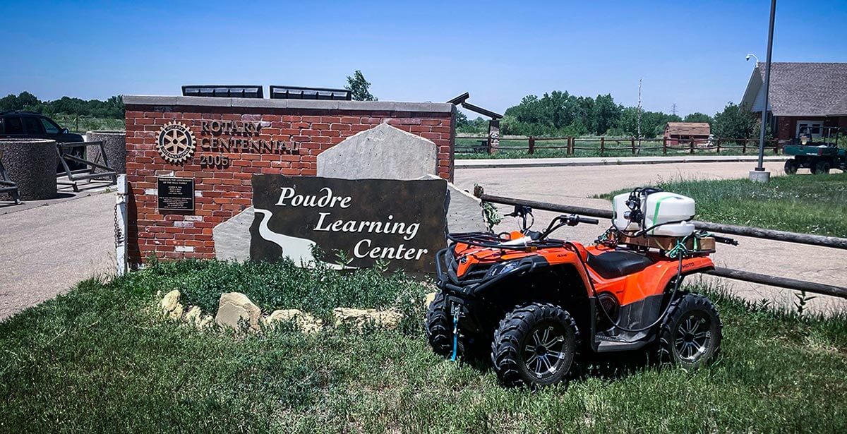 ATV in front of a large brick sign that says "Rotary Centennial 2005, Poudre Learning Center".